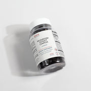 Angled view of the Jeemya Mushroom Extract Complex gummies bottle on a white background, highlighting the dietary supplement packaging and dark gummy contents visible through the transparent bottle.