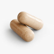 Close-up of two beige The Wow Effect capsules on a white background, highlighting the capsule size, smooth finish, and easy-to-swallow dietary supplement form.