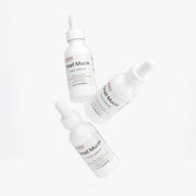 Angled view of multiple Jeemya Snail Mucin Face Serum bottles suspended on a white background, showcasing the product from different perspectives.